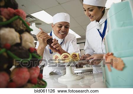 Stock Photograph - Multi-ethnic pastry chefs decorating cake. Fotosearch