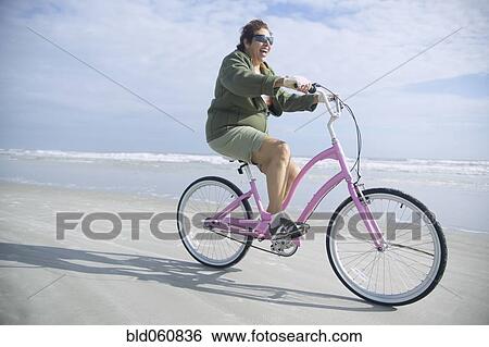 Stock Photograph - Senior Italian woman riding bicycle on beach. Fotosearch