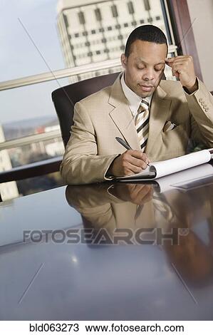 Stock Image - African businessman writing on notepad. Fotosearch