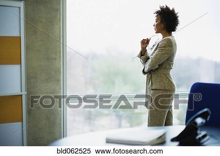 Stock Photography - African businesswoman looking out window in office. Fotosearch