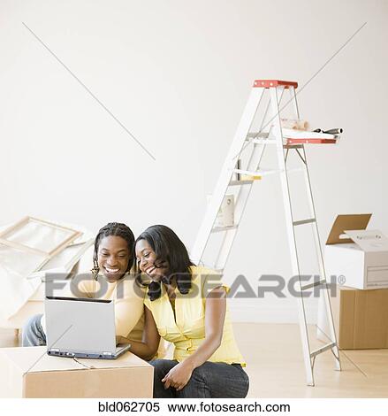Stock Photography - African couple on laptop with moving boxes. Fotosearch