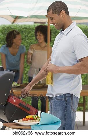 Stock Photograph - African man and women barbecuing. Fotosearch