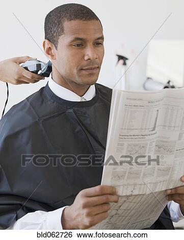 Stock Photograph - African man reading paper at barbershop. Fotosearch