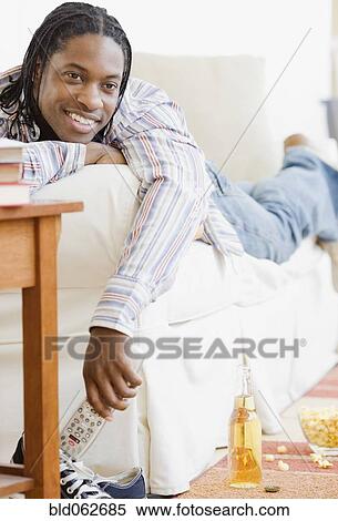 Stock Photography - African man watching television on sofa. Fotosearch