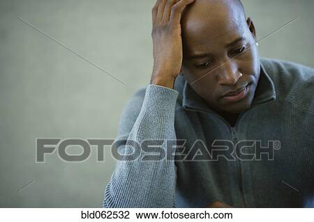 Stock Image - African man with head in hands looking worried. Fotosearch