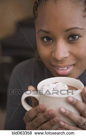 Stock Photo - African woman holding cup of hot cocoa with marshmallows. Fotosearch
