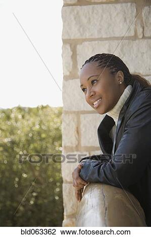 Stock Image - African woman looking at view from balcony. Fotosearch