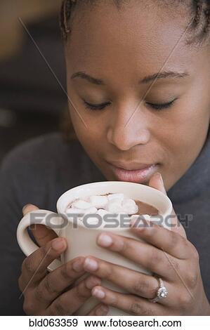 Stock Photo - African woman smelling cup of hot cocoa with marshmallows. Fotosearch