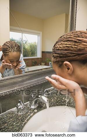 Stock Image - African woman washing face at bathroom sink. Fotosearch