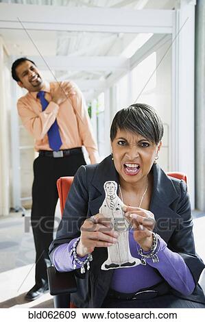 Stock Photo - Angry African businesswoman holding voodoo doll of co-worker. Fotosearch