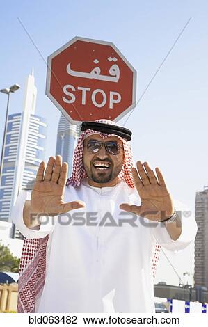 Stock Image - Arab man standing below stop sign. Fotosearch