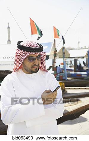 Stock Image - Arab man text messaging on cell phone. Fotosearch