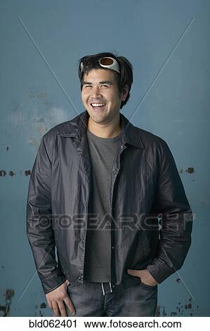 Stock Image - Asian man smiling with hands in pockets. Fotosearch
