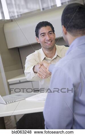 Stock Photo - Businessmen shaking hands in office. Fotosearch