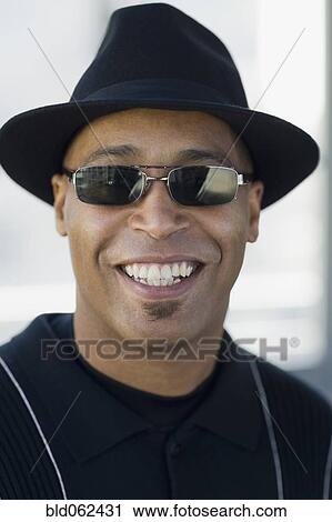 Stock Image - Close up of African man wearing sunglasses and hat. Fotosearch