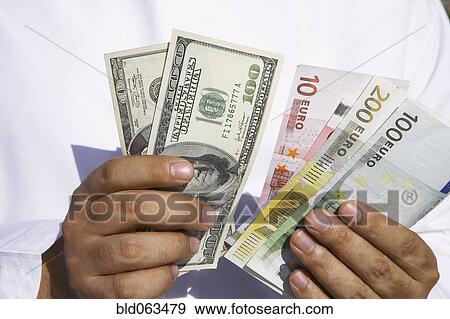 Stock Photo - Close up of Arab man holding dollars and euros. Fotosearch