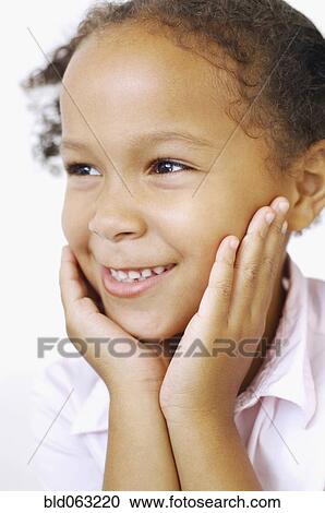 Stock Image - Close up of mixed race girl smiling with head in hands. Fotosearch