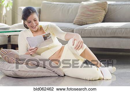 Stock Image - Cuban woman reading magazine on living room floor. Fotosearch