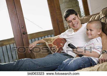 Stock Image - Hispanic father and son watching television on sofa. Fotosearch