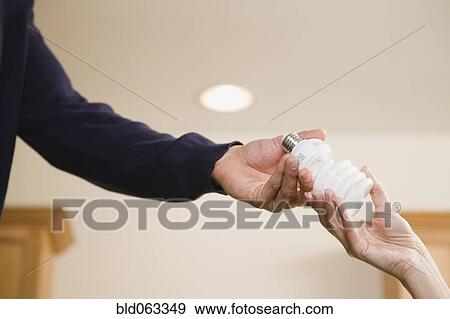 Stock Photo - Hispanic man handing woman compact fluorescent light bulb. Fotosearch