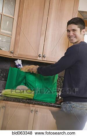 Stock Photo - Hispanic man unloading recyclable shopping bag in kitchen. Fotosearch