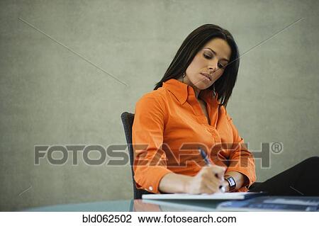 Stock Image - Latin American businesswoman writing in office. Fotosearch