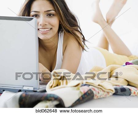 Stock Photo - Middle Eastern woman typing on laptop in bed. Fotosearch
