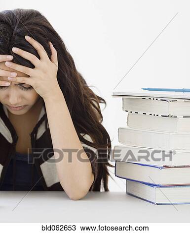 Stock Image - Middle Eastern woman with head in hands next to books. Fotosearch