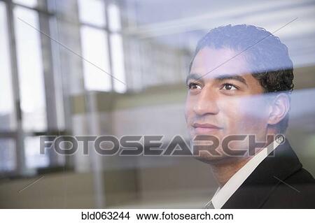 Picture - Mixed race businessman looking through window. Fotosearch