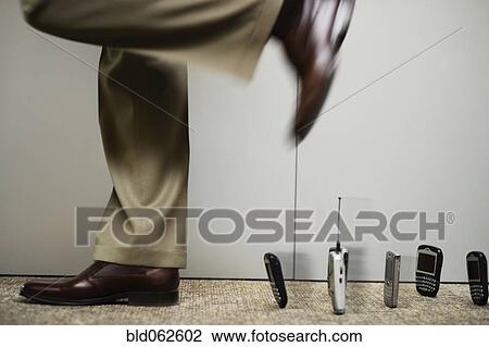 Stock Image - Mixed race businessman stepping over line of cell phones. Fotosearch