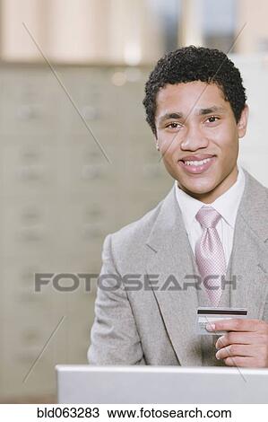 Stock Image - Mixed race businessman with laptop holding credit card. Fotosearch
