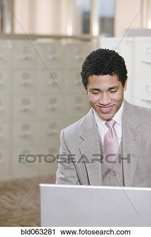 Stock Image - Mixed race businessman working on laptop in office. Fotosearch