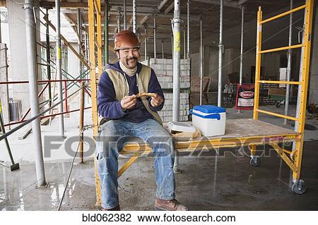 Stock Image - Mixed race construction worker eating lunch. Fotosearch