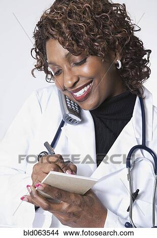 Picture - Mixed race doctor talking on cell phone and taking notes. Fotosearch