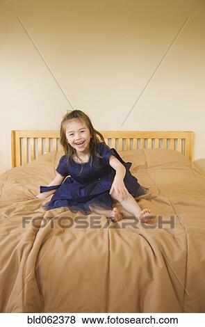 Stock Photo - Mixed race girl in dress laughing on bed. Fotosearch