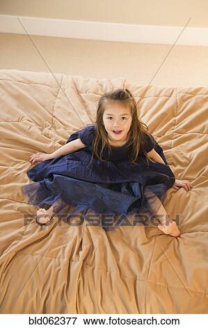 Stock Photo - Mixed race girl in dress on bed. Fotosearch