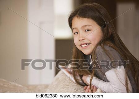 Stock Image - Mixed race girl smiling on sofa. Fotosearch