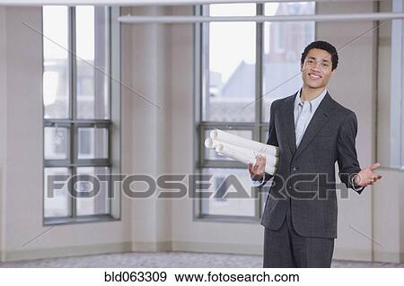 Stock Photo - Mixed race man holding blueprints. Fotosearch