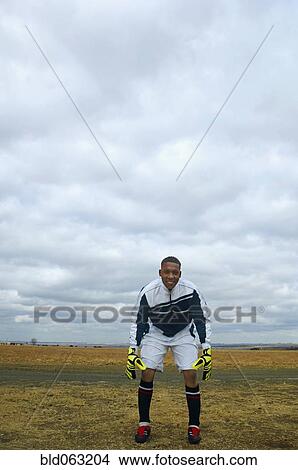 Picture - Mixed race man in soccer uniform standing in remote field. Fotosearch
