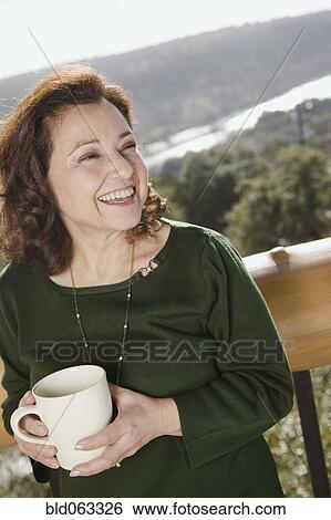Stock Photograph - Mixed race woman holding coffee mug on balcony. Fotosearch