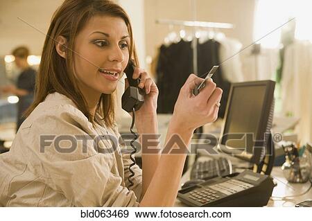 Stock Photo - Mixed race woman holding credit card on telephone in shop. Fotosearch