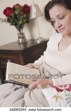 Picture - Mixed race woman reading in bed. Fotosearch