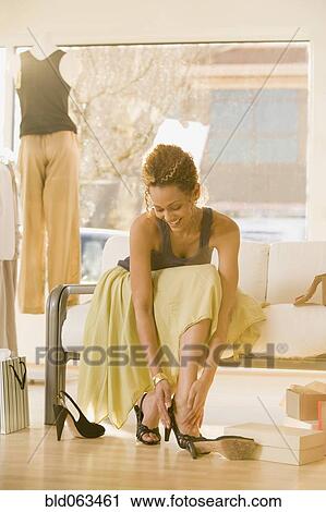 Stock Image - Mixed race woman trying on shoes in shop. Fotosearch
