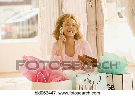 Stock Photo - Mixed race woman with shopping bags talking on cell phone. Fotosearch