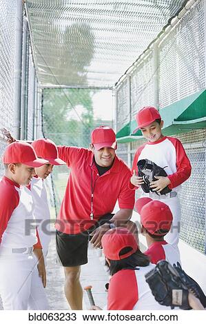 Stock Image - Multi-ethnic boys in baseball uniforms with coach in dugout. Fotosearch