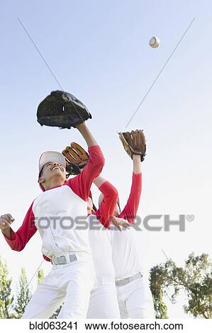 Stock Image - Multi-ethnic boys in baseball uniforms jumping to catch baseball. Fotosearch