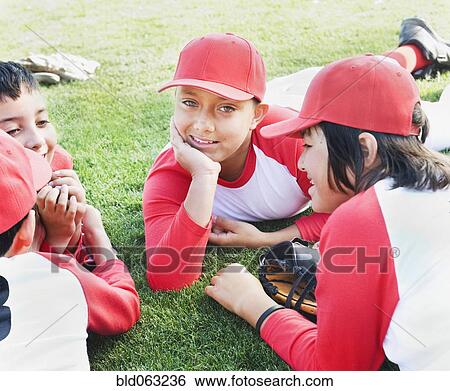 Stock Photograph - Multi-ethnic boys in baseball uniforms laying on grass. Fotosearch