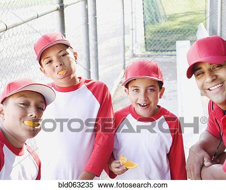 Stock Photography - Multi-ethnic boys in baseball uniforms and coach in dugout eating oranges. Fotosearch