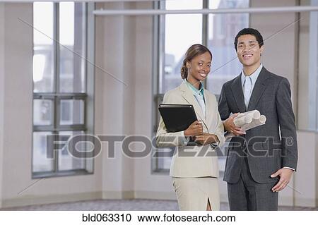 Stock Image - Multi-ethnic business people holding blueprints and binder. Fotosearch