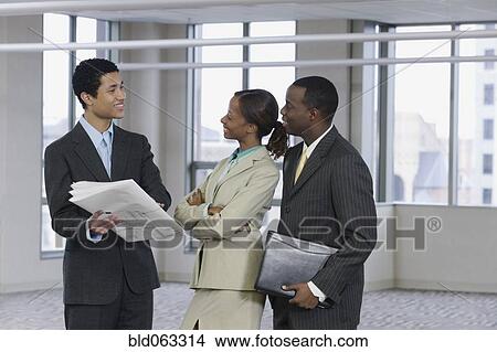 Picture - Multi-ethnic business people reviewing blueprints. Fotosearch